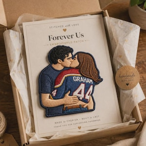 May include: An embroidered patch featuring a couple kissing, with the person on the right wearing a blue jersey with the name GRAHAM and the number 44. The patch is mounted on a card inside a cardboard box with the text STITCHED with LOVE Forever Us.