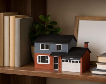 May include: A miniature house model with a blue and red exterior, black roof, and white garage door. The model sits on a wooden shelf with books and a framed picture. A small plant is also on the shelf.