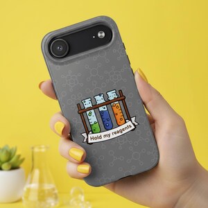 May include: A gray phone case featuring a cartoon illustration of three colorful test tubes in a wooden rack. The test tubes contain green, blue, and orange liquids. The phrase "Hold my reagents" is written on a banner below the rack.