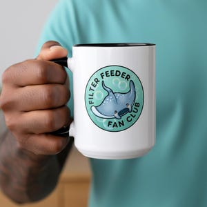 May include: A white ceramic mug with a black handle and the text "But First, Coffee" in a black, handwritten-style font. The mug is on a white surface.