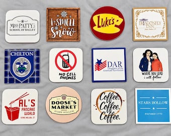 Op de afbeelding: Een set van twaalf vierkante en ronde onderzetters met diverse grafische ontwerpen en teksten, waaronder Miss Patty's School of Ballet, I Smell Snow, Luke's, Dragonfly Inn, Chilton, No Cell Phones, DAR, Where You Lead, Al's Pancake World, Doose's Market, Coffee Coffee Coffee en Stars Hollow.