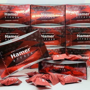 May include: Red and silver boxes of Hamer ginseng and coffee. The boxes have the text "Hamer 37 F8 2 K GINSENG + COFFEE" printed on them. Individual packets are scattered in front of the boxes. The website address www.hamer2u.com is also visible.