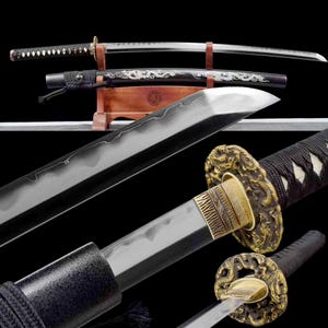 Op de afbeelding: Een assortiment Japanse zwaarden, waaronder een katana en een wakizashi, gepresenteerd op een houten standaard. De bladen zijn zilverkleurig, met sierlijke gouden en zwarte handvatten. De scheden zijn zwart met drakenontwerpen.