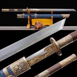 May include: An ornate sword with a straight, silver blade. The hilt and scabbard feature intricate gold-colored designs. The handle is wrapped in brown material, and the scabbard is blue. The sword rests on a wooden stand.