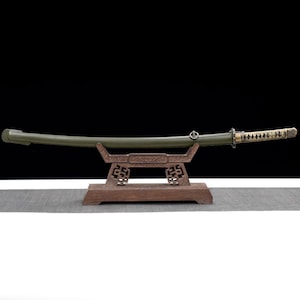 May include: A Japanese katana sword with a green scabbard and a decorative handle, resting on a wooden stand. The blade is slightly curved, and the handle features a diamond pattern. The stand has an ornate design.