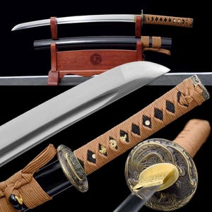 Puede incluir: Dos espadas katana japonesas con hojas plateadas y empuñaduras marrones. Una espada está envainada en una vaina negra, expuesta en un soporte de madera. Las empuñaduras presentan intrincados patrones de diamantes y adornos metálicos decorativos.