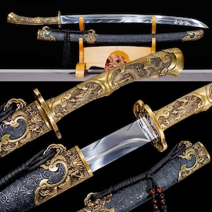 May include: An ornate sword with a curved blade and a gold-colored handle and scabbard. The handle and scabbard are intricately detailed with dragon motifs. The sword is displayed with its scabbard on a wooden stand.