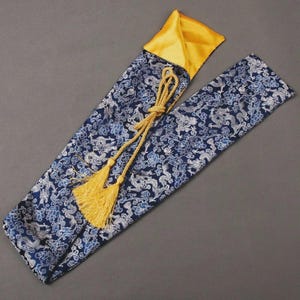 May include: A blue and white patterned fabric sheath with a yellow satin lining and a gold tassel. The sheath is open, revealing the yellow interior. The fabric features a repeating pattern of stylized clouds and dragons.