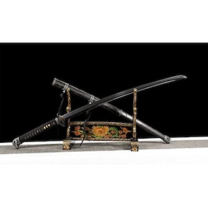 May include: A black katana sword with a matching scabbard resting on a decorative black and gold stand. The stand features a central floral motif with green leaves and yellow petals, while the sword handle is wrapped in black cord with silver accents.