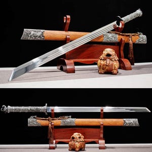 May include: A pair of swords with wooden scabbards and decorative handles. The blades are silver and the scabbards are brown with silver accents. A small, brown, ceramic lion statue sits in front of the swords.
