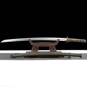May include: A Japanese katana sword with a curved blade, displayed on a wooden stand. The hilt is gold and black, and the scabbard is olive green. The sword is a traditional weapon.