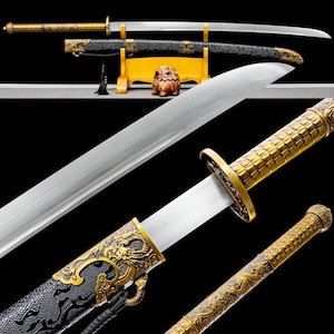 May include: A detailed image of a traditional sword with a curved blade. The sword features a gold-colored hilt and scabbard with intricate dragon and geometric designs. The blade is silver, and the scabbard is black with gold accents. The sword is displayed on a wooden stand.