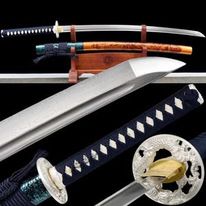 Op de afbeelding: Twee Japanse katana-zwaarden worden getoond. De bladen zijn zilverkleurig met ingewikkelde patronen. De handvatten zijn gewikkeld in donkerblauwe stof met witte ruitpatronen. Eén zwaard zit in de houten schede, die een gedetailleerd ontwerp heeft.