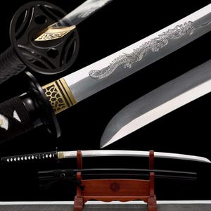 Puede incluir: Una espada katana japonesa con una hoja plateada y un grabado detallado de un dragón. La empuñadura es negra con detalles dorados, y la espada descansa sobre un soporte de madera. El diseño es tradicional y ornamentado.