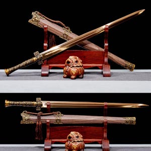 May include: A golden-hued sword with an ornate handle and a wooden scabbard. The sword is displayed on a wooden stand, with a decorative ceramic lion figurine in the foreground. The blade has a long, straight edge.