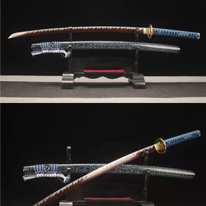 Op de afbeelding: Twee Japanse katana-zwaarden met sierlijke handvatten en scheden. De bladen hebben een roodbruine tint met een gekartelde rand. De handvatten zijn blauw en goud, en de scheden zijn zwart met een gespikkeld patroon. De zwaarden worden op een zwarte standaard getoond.