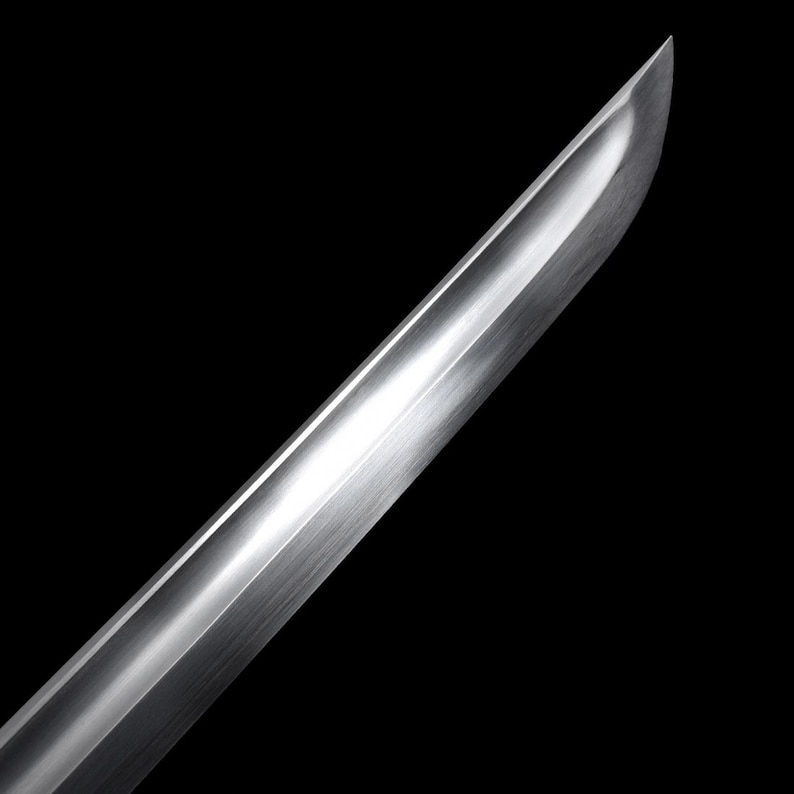 May include: Close-up of a polished, silver-colored sword blade against a black background. The blade has a curved edge and a reflective surface, catching the light. The image highlights the craftsmanship and sharpness of the weapon.