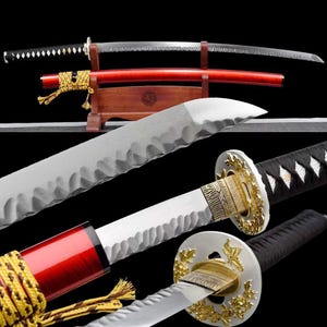 May include: A display of Japanese katana swords. One sword is sheathed in a red scabbard, while another is unsheathed, revealing a silver blade with a distinctive edge. The handles are black and white, with gold accents.
