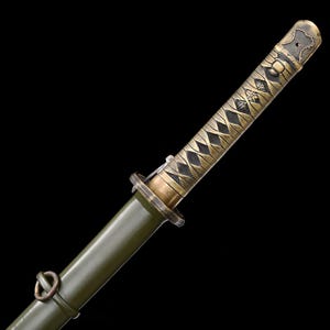 May include: Close-up of a Japanese katana sword. The handle is wrapped in a diamond pattern with a gold finish. The scabbard is olive green. The sword's hilt and fittings have an antique gold finish. The blade is not visible.