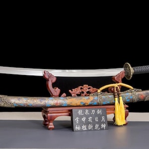 May include: A decorative sword with a curved blade, resting on a wooden stand. The scabbard is ornate with colorful designs. A small sign with Chinese characters is in front of the sword.