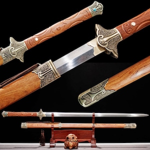 May include: An ornate sword with a wooden handle and scabbard. The handle is intricately carved and features a decorative metal guard. The blade is silver and sharp. The scabbard is also wooden with metal accents. The sword is displayed on a wooden stand.
