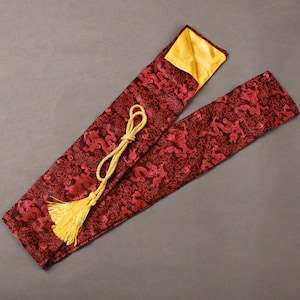 Peut inclure: Un étui en tissu à motifs rouges et noirs avec un gland et un cordon dorés. L'étui a un intérieur jaune et est conçu pour contenir un objet long et fin. Le tissu présente un motif de dragon.