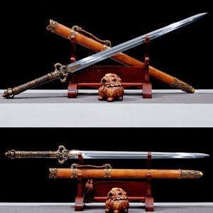 May include: An ornate sword with a polished steel blade and a decorative bronze handle and scabbard. The wooden scabbard is brown with bronze accents. The sword rests on a wooden stand with a small decorative statue.