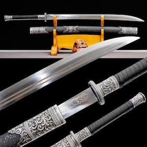 May include: An ornate sword with a silver blade and decorative handle. The blade has three parallel lines etched into it. The handle is black with silver filigree. The sword is displayed on a wooden stand.