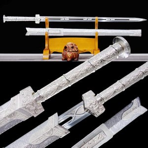 May include: A silver-colored sword with intricate carvings and a decorative handle. The sword is displayed on a wooden stand, showcasing its detailed design and craftsmanship. The blade is long and sharp, with a protective sheath.