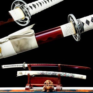 May include: An assortment of Japanese katana swords. The blades are a deep red, with white and silver accents on the handles and sheaths. One sword is displayed in a wooden stand, showcasing intricate dragon artwork.