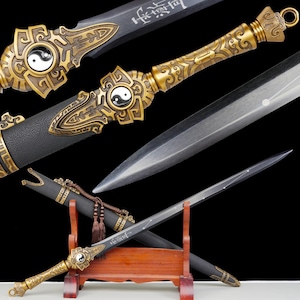 May include: A detailed image of a decorative sword with a black blade and a gold-colored handle. The handle features intricate designs and a yin-yang symbol. The sword is displayed on a wooden stand.
