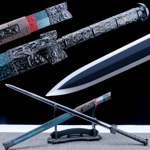 May include: An ornate, silver-colored sword with a black blade and a decorative handle. The scabbard is teal and silver with red accents. The sword is displayed on a black stand.