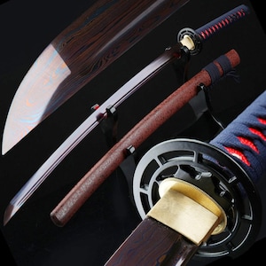 May include: A Japanese katana sword with a curved blade and a brown handle. The blade has a unique pattern, and the handle is wrapped in blue and red fabric. The sword is displayed on a black stand.