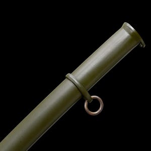 May include: Olive green metal scabbard with a circular ring and a band. The scabbard has a cylindrical shape and a slightly flared opening. The background is black.