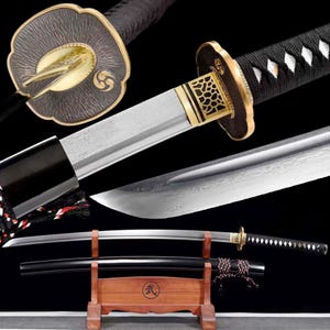 Op de afbeelding: Een Japanse katana-zwaard met een gebogen lemmet, zwarte handgreep en sierlijke goud-zwarte beschermer. Het lemmet heeft een gedetailleerd patroon. Het zwaard rust in een houten standaard met het Japanse symbool voor vechtsporten.