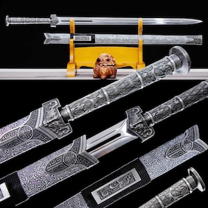 May include: An ornate silver sword with a polished blade, displayed with its scabbard on a wooden stand. The hilt and scabbard are intricately detailed with engraved patterns and dragon motifs. A small, brown decorative figurine sits nearby.