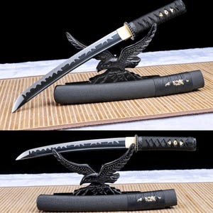 May include: A Japanese katana sword with a black handle and scabbard, displayed on a black eagle-shaped stand. The blade has a distinctive wavy edge. The sword is a traditional weapon.