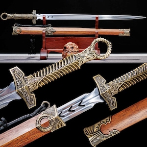 May include: An ornate sword with a silver blade and a decorative bronze handle. The sword is displayed on a wooden stand with a matching scabbard. The handle features intricate carvings and a ring-shaped pommel. The blade has etched arrow markings.