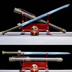 Peut inclure: Deux épées ornées avec des lames bleues et des poignées et fourreaux décoratifs sont exposées sur un support en bois rouge. Un petit objet décoratif marron sculpté est placé sous les épées. Les épées ont des détails dorés complexes.