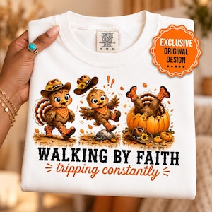 May include: A white crewneck t-shirt featuring a graphic of three cartoon turkeys wearing cowboy hats and boots. One turkey is walking, one is jumping, and one is inside a pumpkin. The text reads "WALKING BY FAITH tripping constantly".