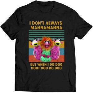 May include: Black t-shirt with a graphic of three Muppet-like characters. The text reads "I DON'T ALWAYS MAHNAMAHNA" above the image, and "BUT WHEN I DO DOO DOOT DOO DO DOO" below. The creatures are pink, orange, and green, set against a striped background.