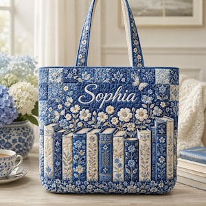 May include: A quilted tote bag in shades of blue and white, featuring the name Sophia embroidered in white script. The design includes floral patterns, butterflies, and a row of vertical book spines along the bottom with two shoulder straps.
