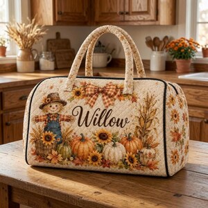 Peut inclure: Un sac de voyage matelassé avec un imprimé automnal représentant un épouvantail, des citrouilles, des tournesols et des tiges de maïs. Le prénom Willow est écrit en lettres cursives au centre, orné d'un nœud à carreaux, deux anses et bordure noire.