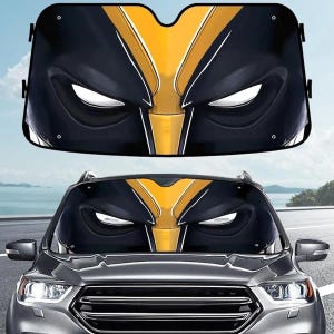 May include: A rectangular car windscreen sun shade featuring a graphic print of a black and yellow mask with stylised white eye cutouts. The design mimics a superhero face with sharp angular lines and a central yellow vertical stripe.