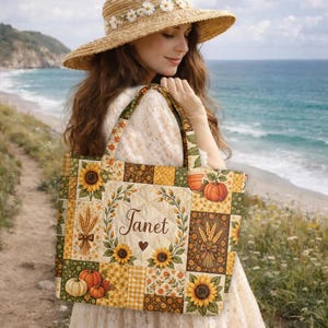 May include: A quilted tote bag featuring a patchwork design of sunflowers, wheat stalks, and pumpkins in shades of orange, yellow, and green. The centre panel displays the name Janet in cursive script surrounded by a leafy wreath and a small heart.