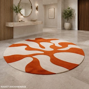 May include: A round rug with an abstract design in orange and cream. The rug features a swirling pattern of orange shapes against a cream background. The rug is placed on a tiled floor in a modern interior setting.