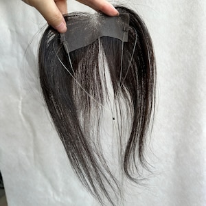 May include: A dark brown hair extension piece featuring a rectangular mesh base with a thin, clear wire loop attached for secure placement. The straight, smooth hair strands hang downward from the mesh, creating a natural layered appearance.