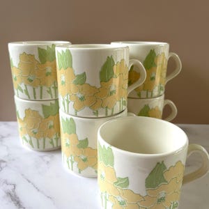 May include: A set of three ceramic mugs with a speckled, matte finish. The mugs are in shades of cream, light grey, and dark grey. Each mug has a simple, minimalist design, ideal for coffee or tea.