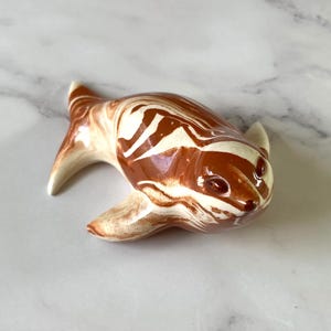 May include: A ceramic seal figurine with a brown and cream marbled design. The seal has a curved body, flippers, and a small head with dark eyes. The figurine is a decorative item.