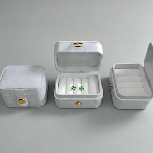 May include: Three white jewelry boxes with gold clasps are displayed. One box is closed, another is open with two green clover earrings inside, and the third is open. The text "gift box" is at the bottom.